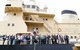Ein Ausschnitt von einem beigefarbenen Schiff, an der Reling stehen viele Menschen in "Business"-Kleidung und schauen in die Kamera. Es sind die Mitglieder der Delegation.