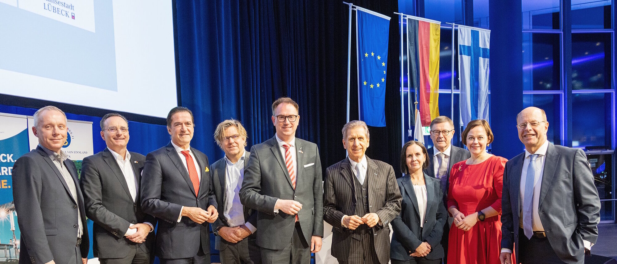 Eine Gruppe von zehn Menschen, die auf einer Bühne nebeneinander stehen. Zwei davon sind Frauen.